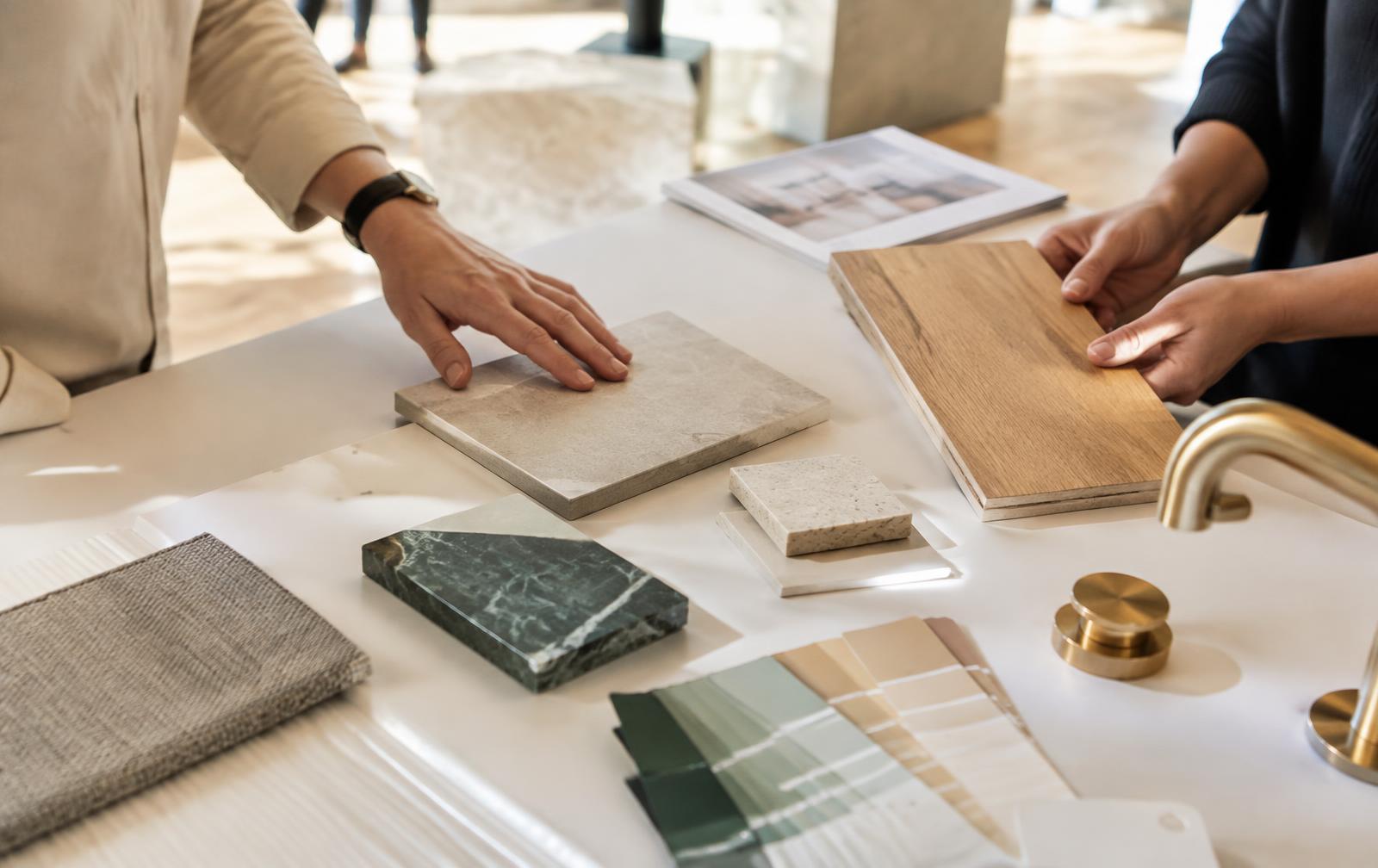 Hands comparing tile, wood and paint samples on a table